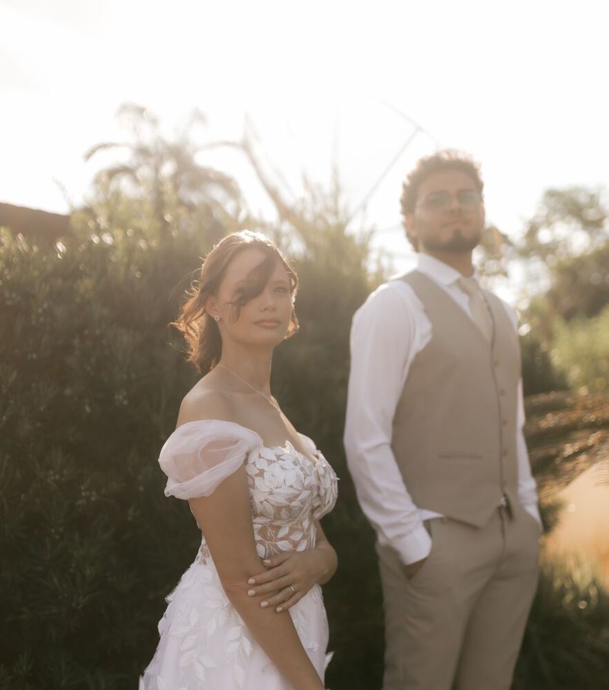 Bride and groom standing by a hedge in evening light
